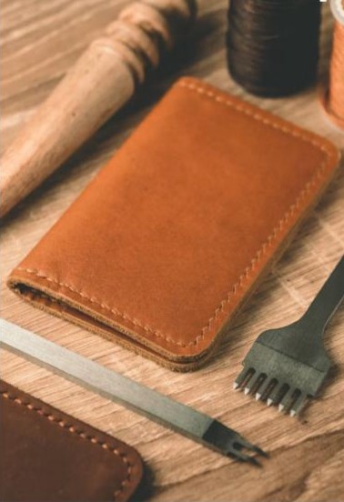 Hand-stitched leather wallet with craftsman's tools and thread